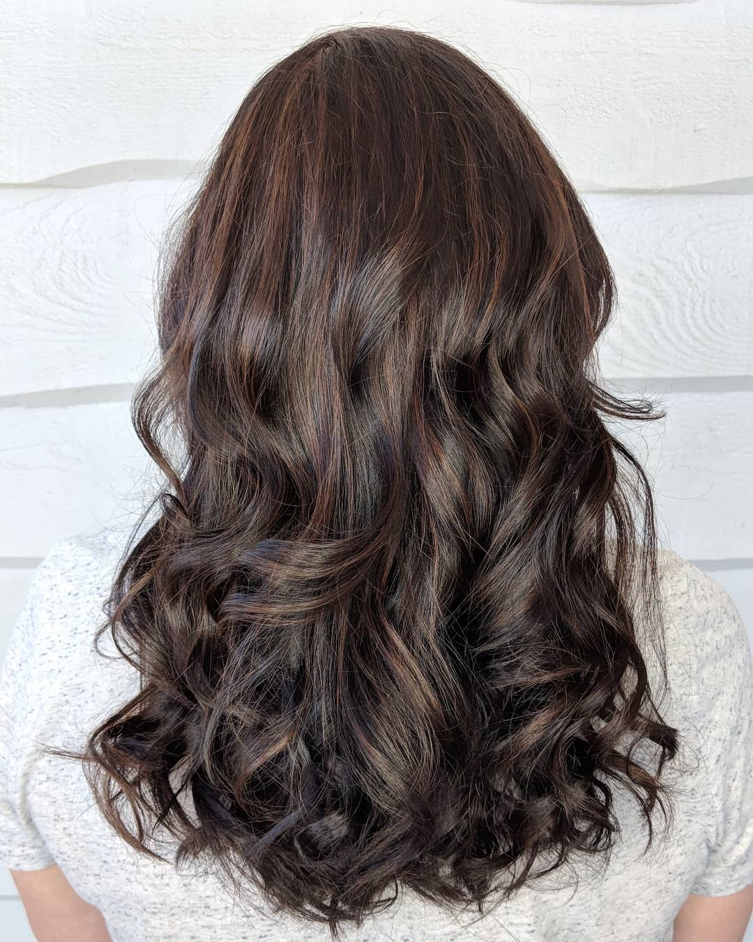 Woman with medium length curly brunette hair with mahogany highlights